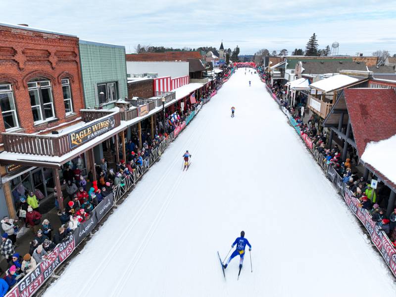 Cross-country skiers racing down a snow-covered main street during the American Birkebeiner in Cable, Wisconsin.